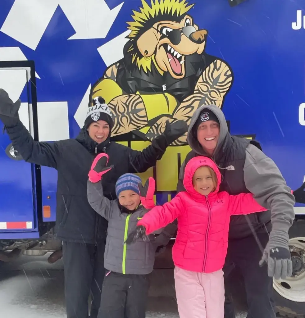 A family waving in the snow in front of Hauler on the side of a Junk Punk truck
